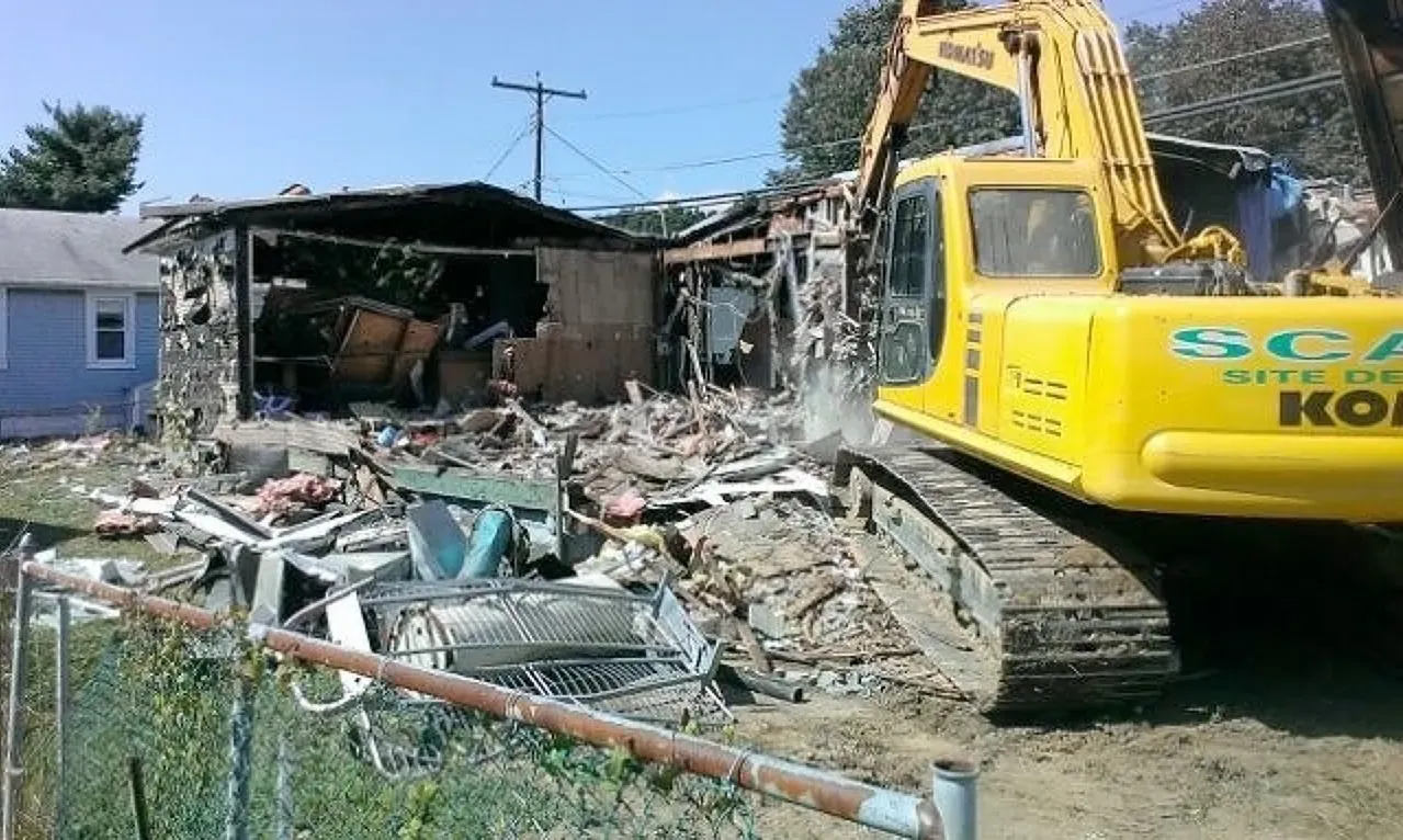 A yellow kobelco excavator is demolishing a house.