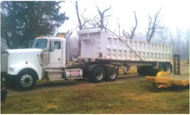 A white dump truck is parked in a grassy field.