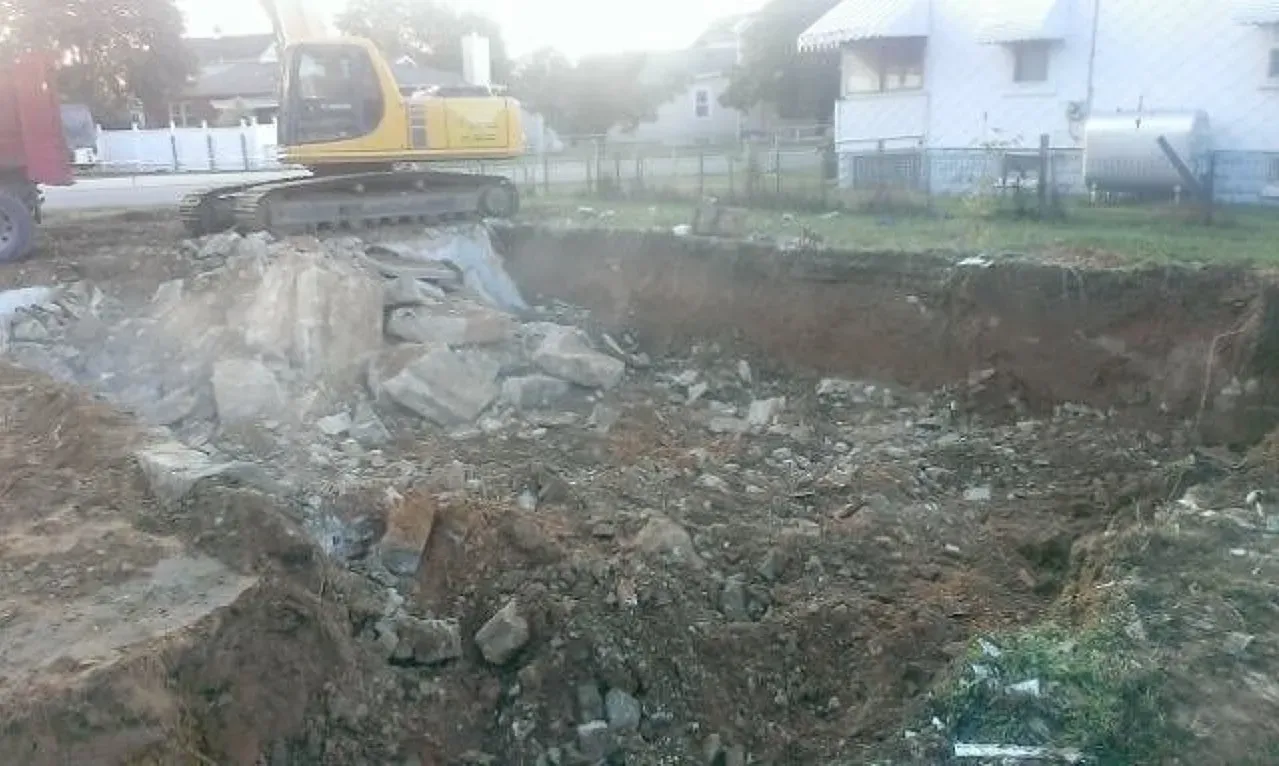 A yellow excavator is digging a hole in the dirt in front of a house.