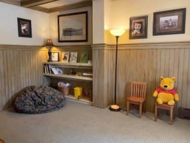 Cozy reading nook with beanbag chair, wooden shelves with books, stuffed Winnie the Pooh, and framed artwork.