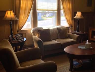 Cozy living room with a couch and armchair. Two lamps flank the couch and a window with blinds.