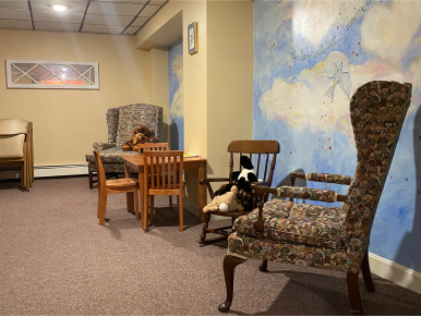 A child's play area with furniture: table, chairs, armchairs, and a rocking chair, with a sky-themed mural.