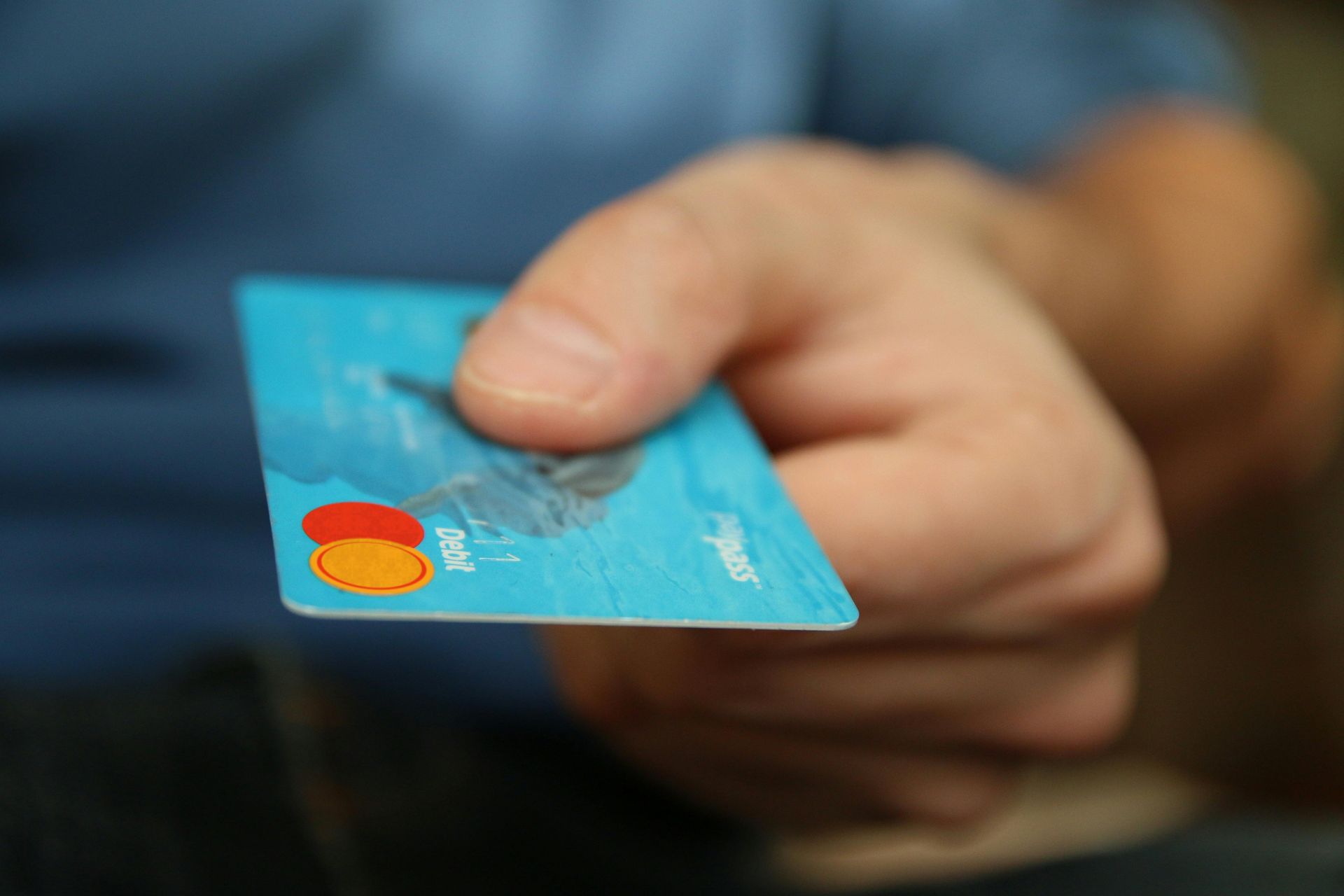 Hand holding a light blue credit card with the Mastercard logo.
