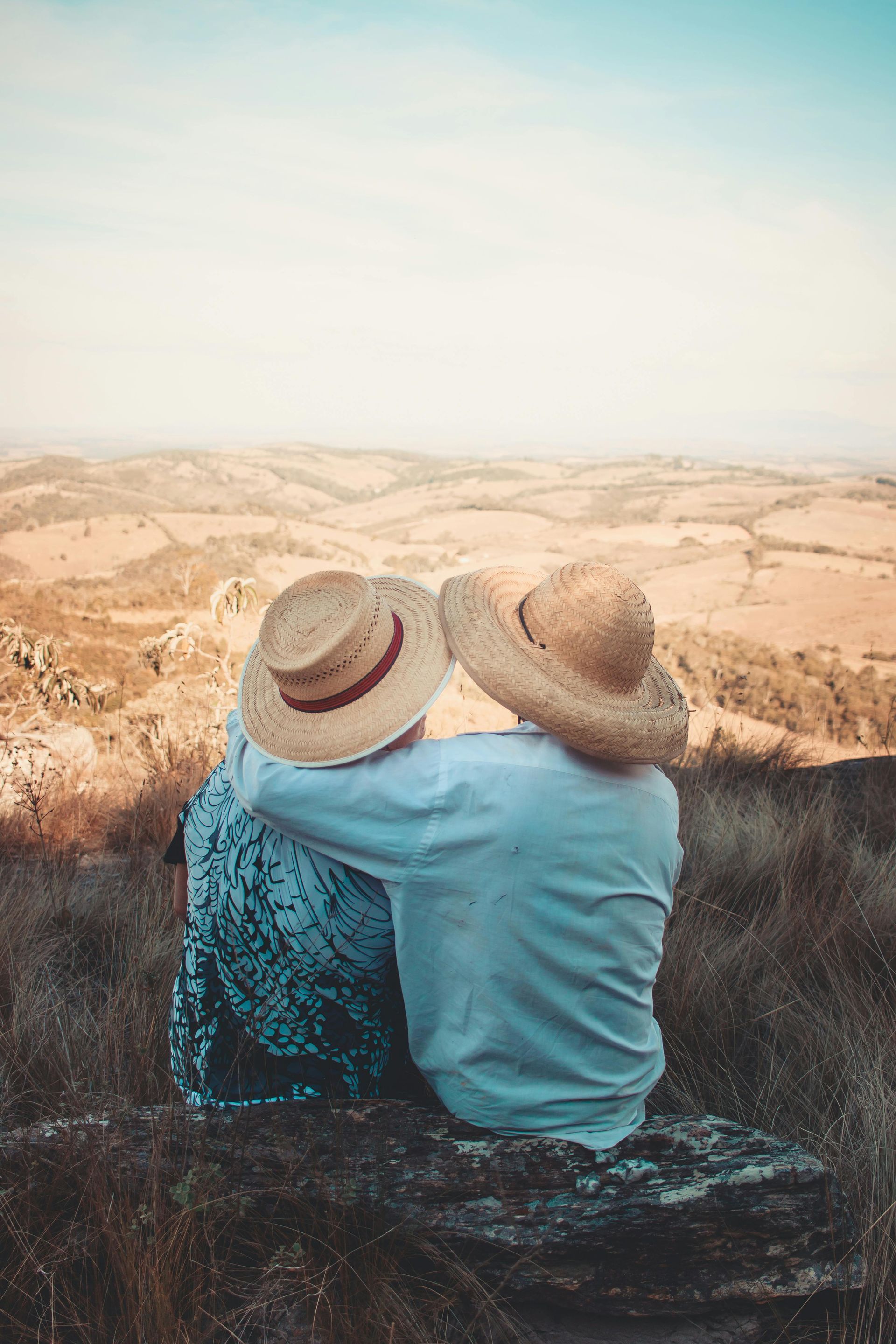 Two people in straw hats embrace, overlooking a rolling, dry landscape.
