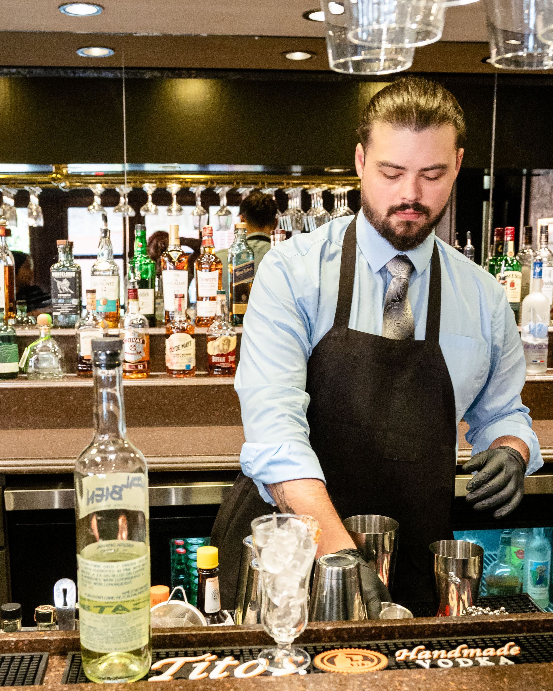 A bartender prepares a drink in front of a bottle of tito 's vodka