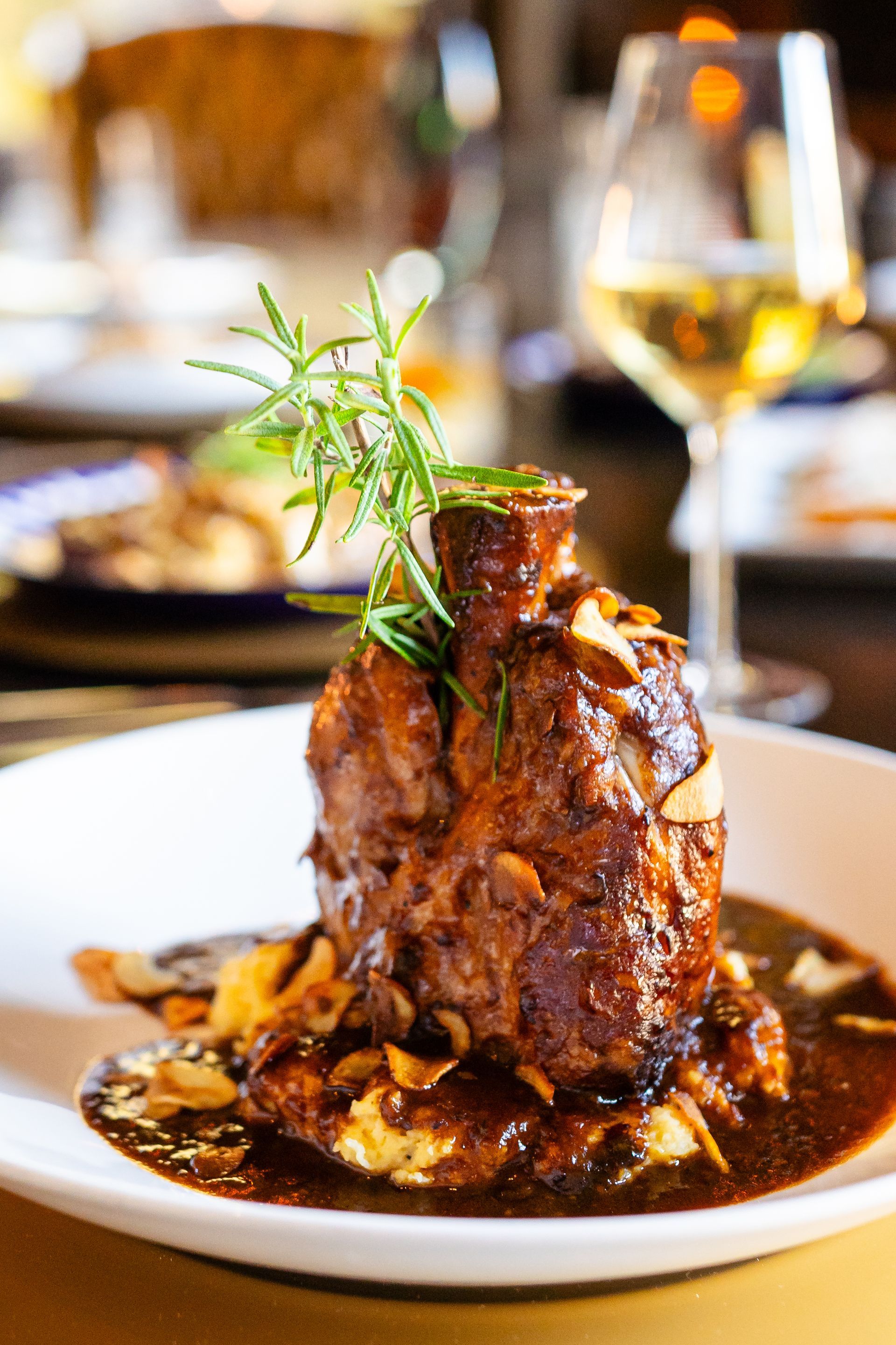 A close up of a plate of food with a glass of wine in the background.