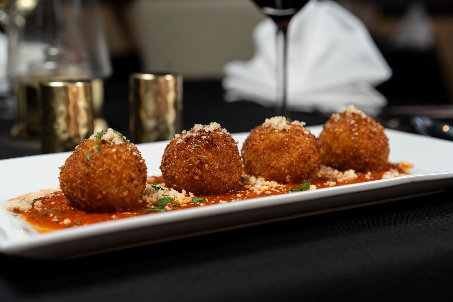A close up of a plate of food on a table with a glass of wine in the background.