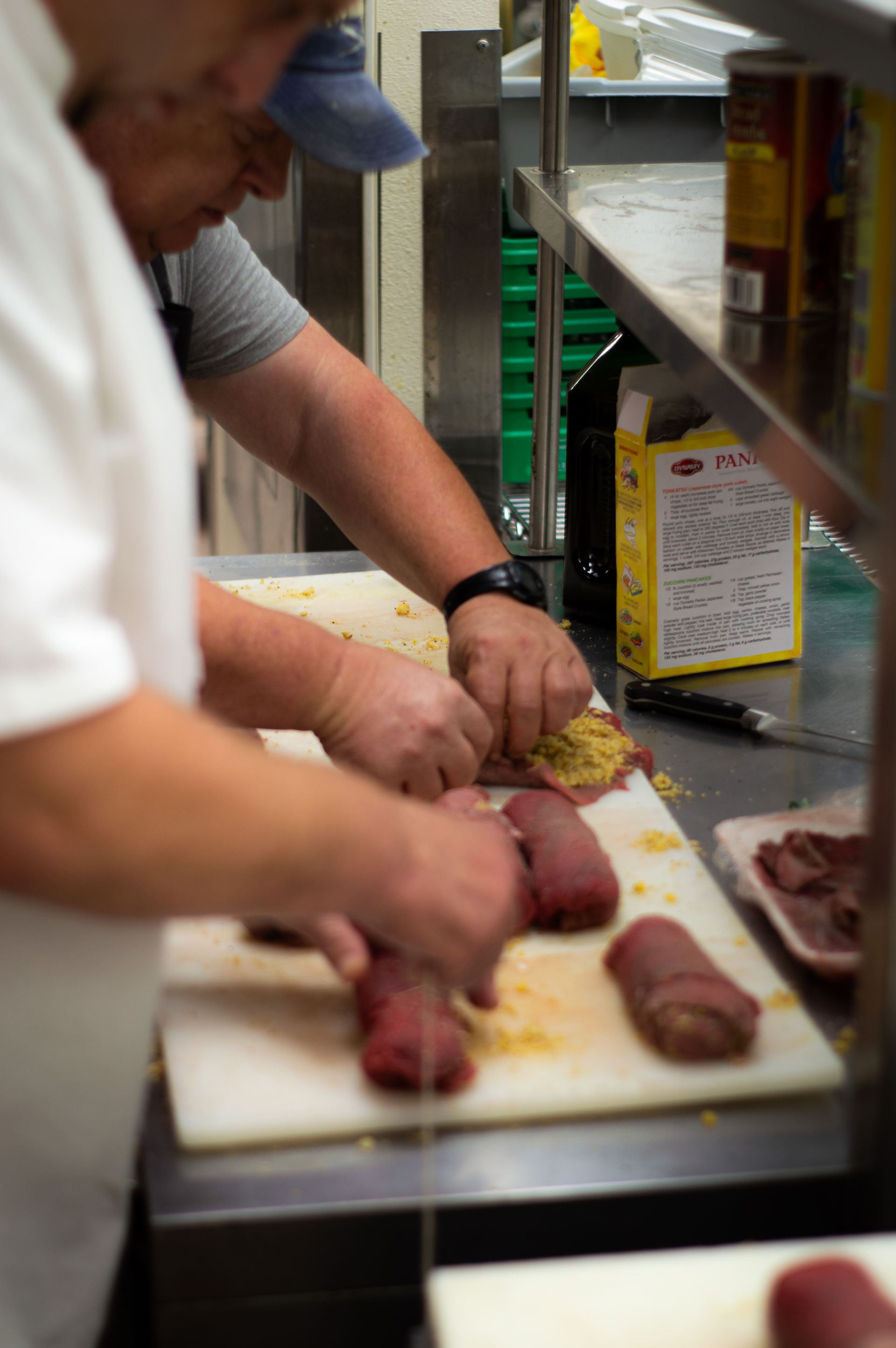 Two men are cutting meat on a cutting board in a kitchen.