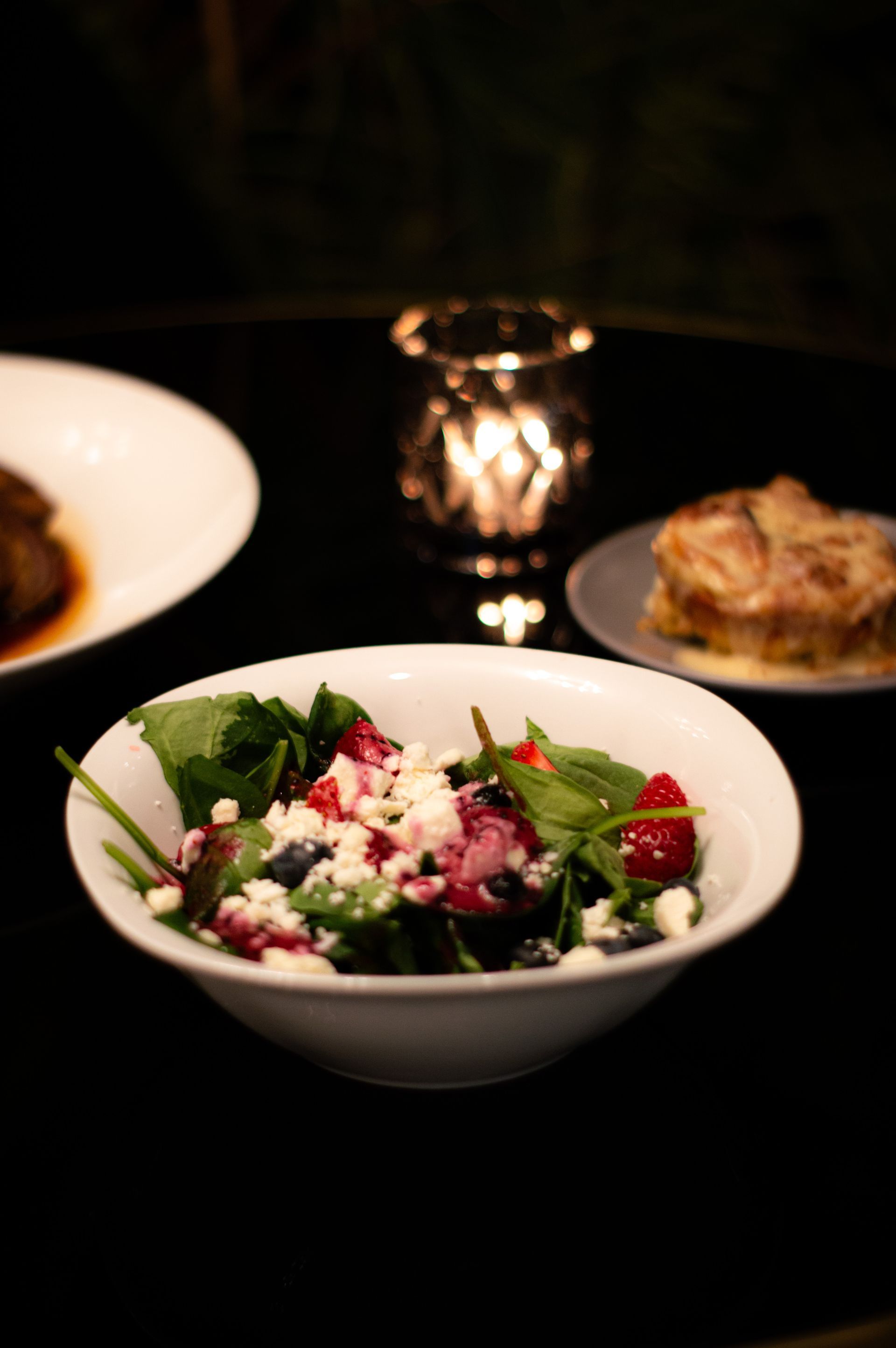 A bowl of salad is sitting on a table next to plates of food.