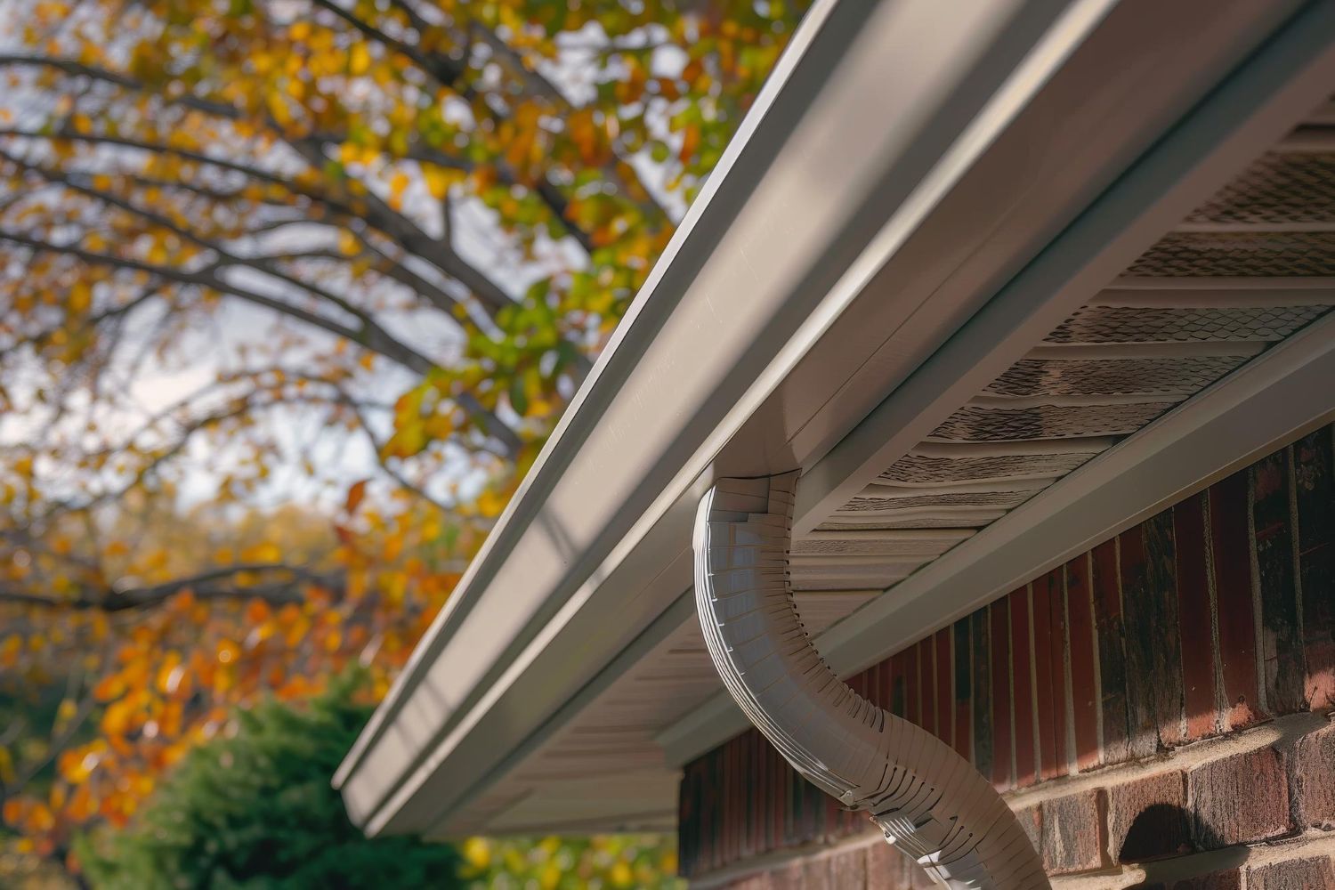 A close up of a gutter on a brick house with trees in the background.