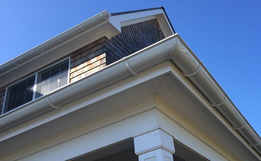 The roof of a house with a white gutter and a blue sky in the background.