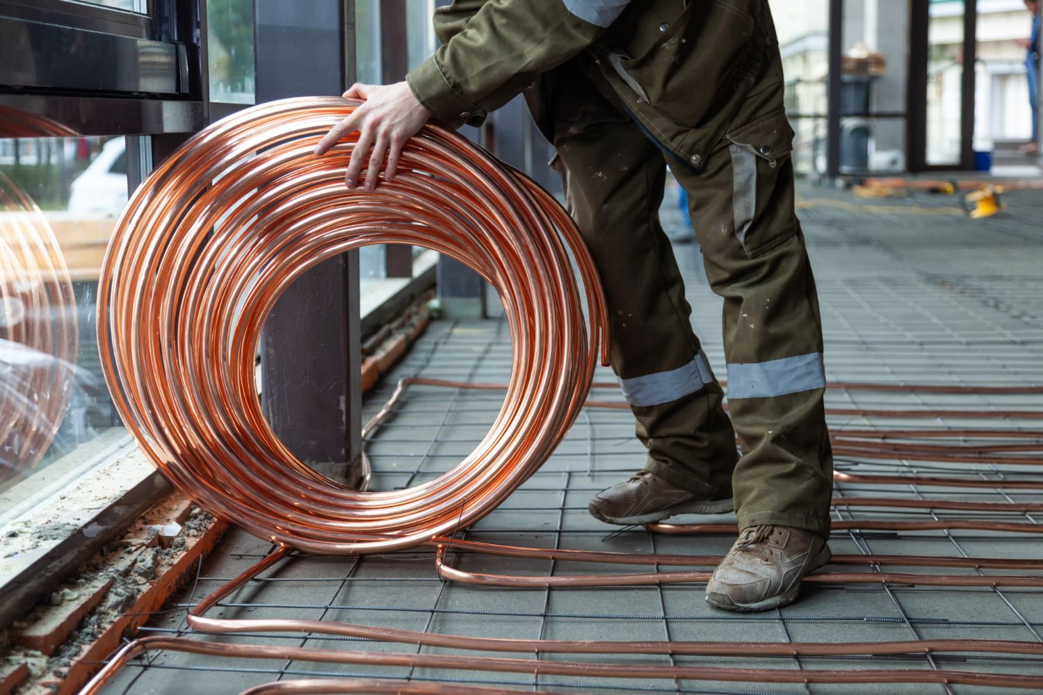 A man is holding a large roll of copper pipe.