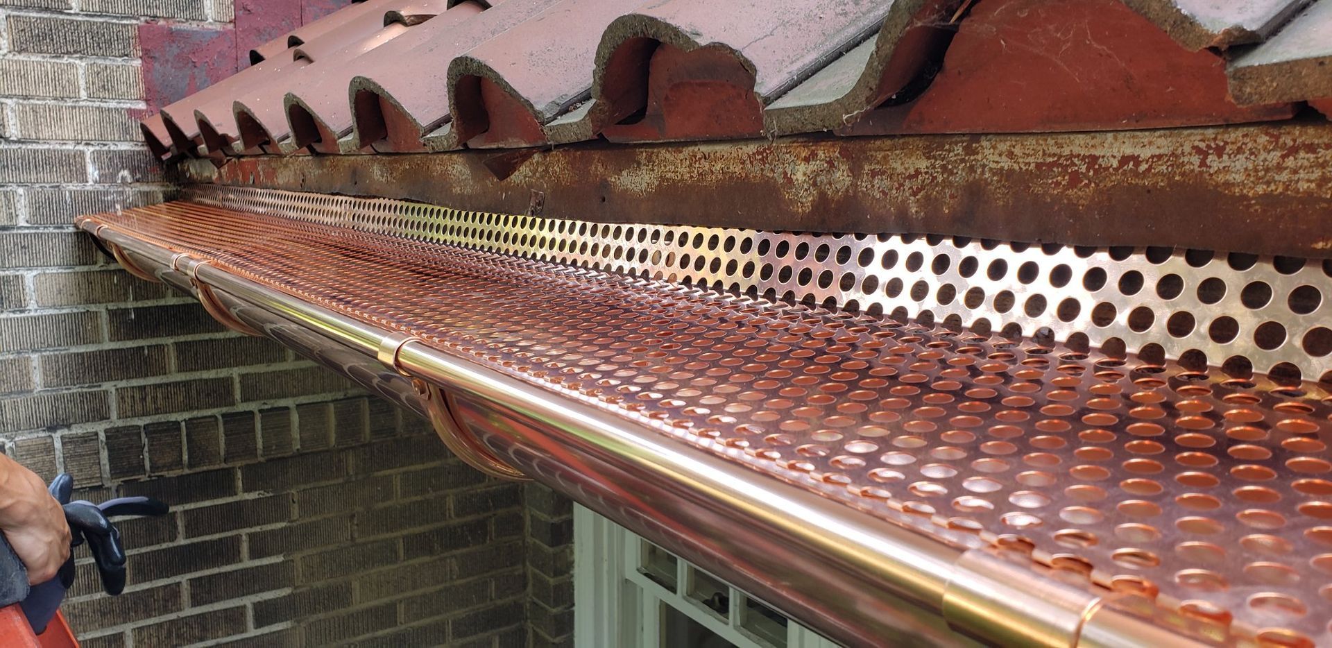 A person is working on a copper gutter on the side of a building.