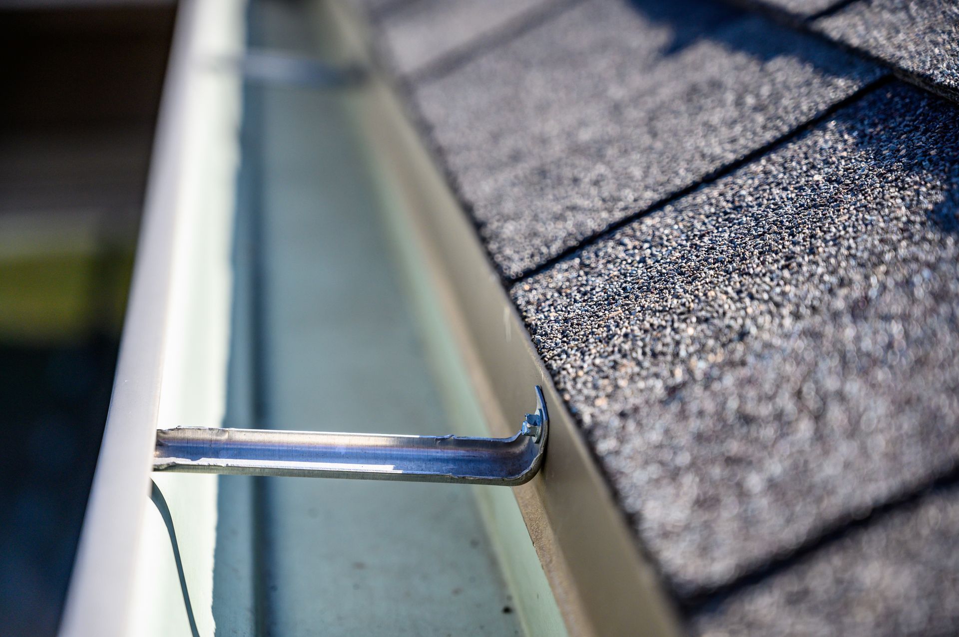 A close up of a gutter on a roof with a metal hook attached to it.