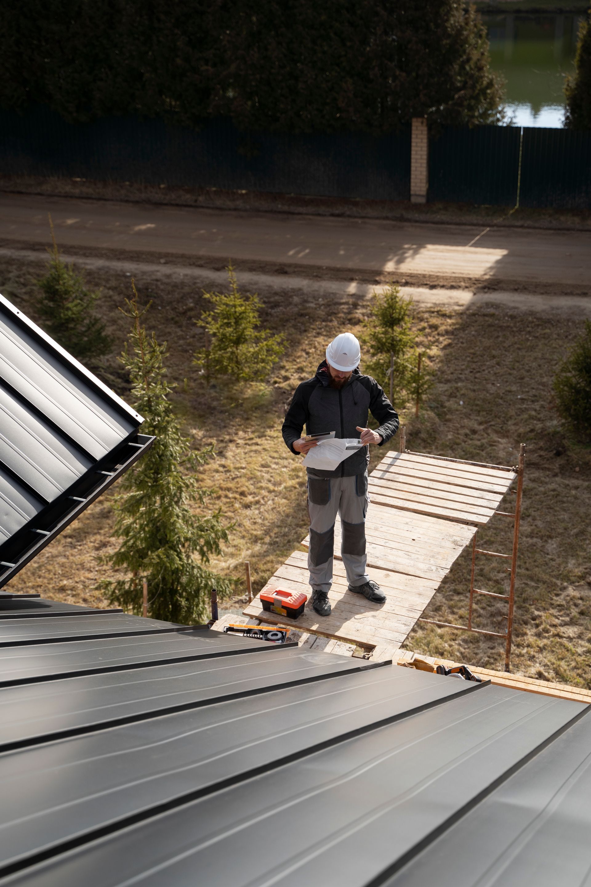 A man is standing on top of a roof looking at a clipboard.