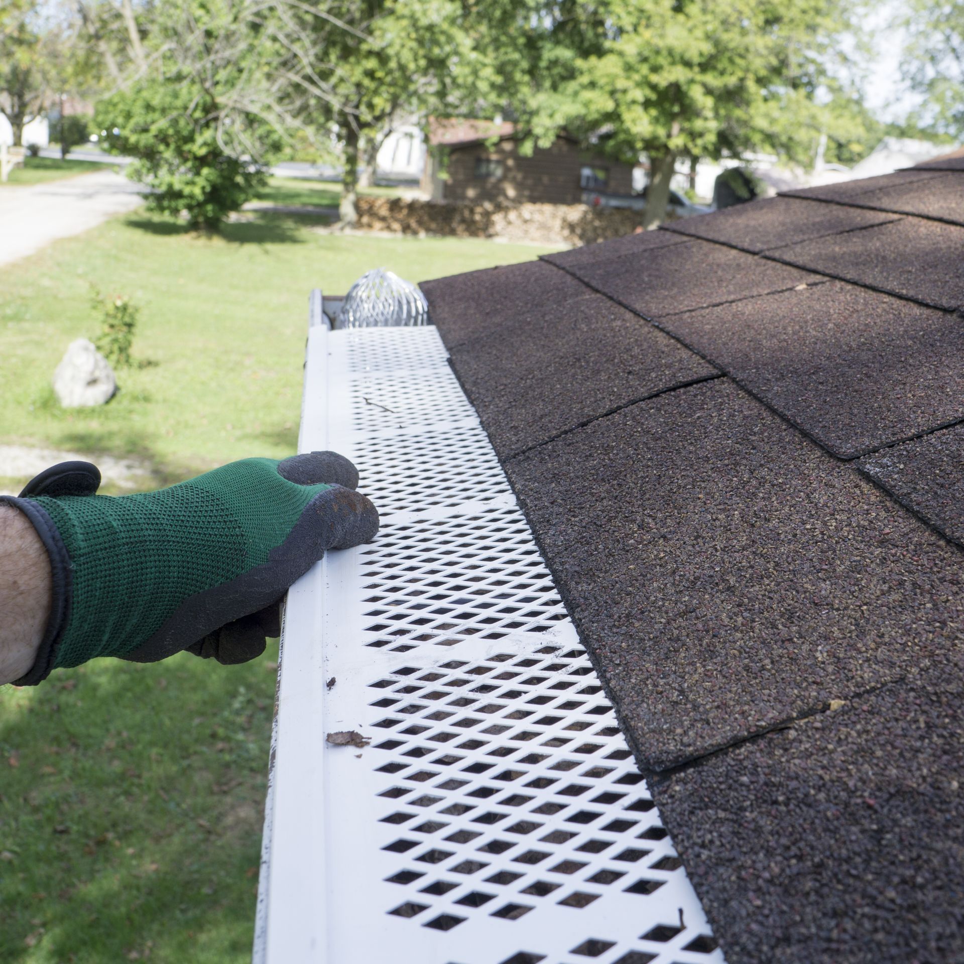 A person wearing green gloves is cleaning a gutter on a roof