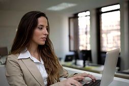 A woman is typing on a laptop computer in an office.