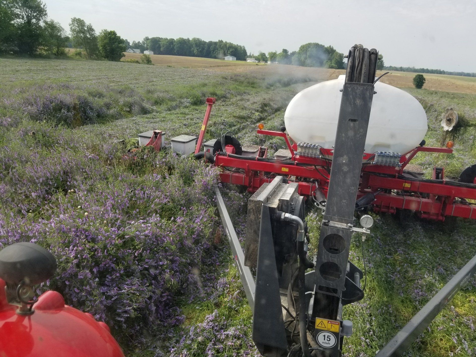 A tractor spraying a field of purple-flowered plants. A large white tank is visible.