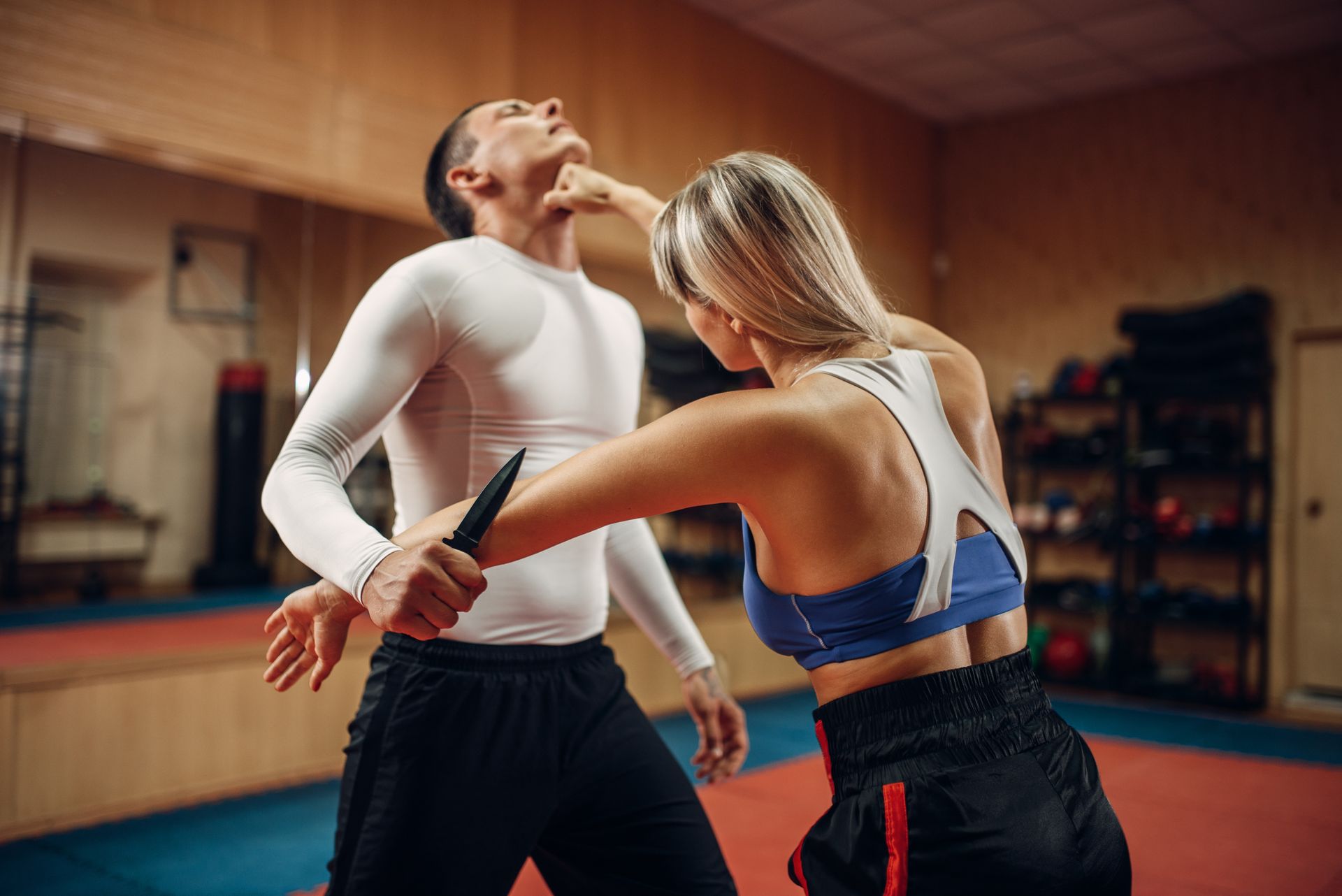 A man and a woman are wrestling on a mat in a gym.