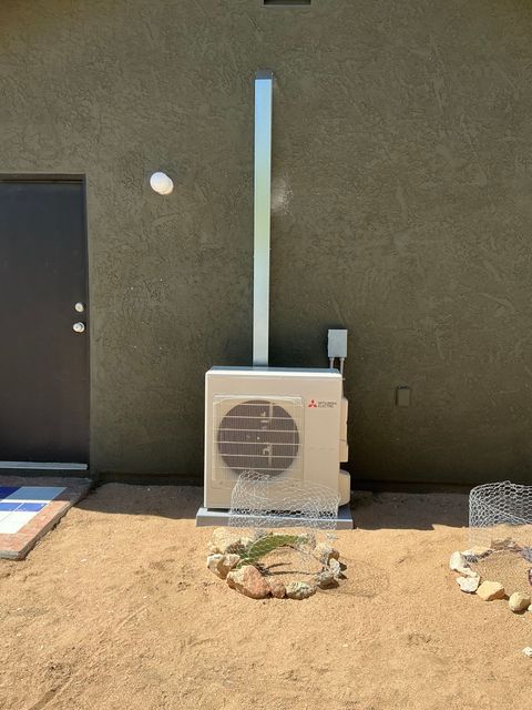 Outdoor air conditioner unit against a wall with a vertical blue pipe and gravel ground