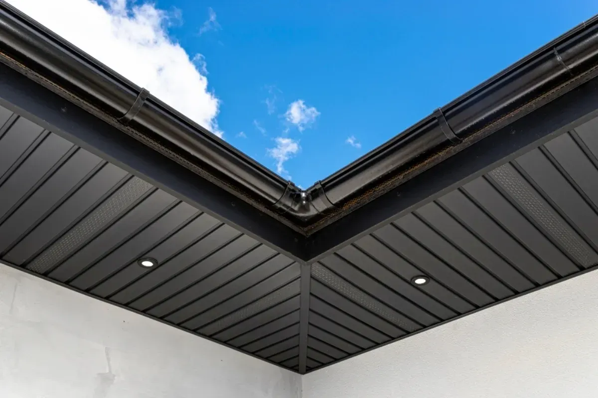An upward view of a corner of a building roof with black-paneled soffits, integrated LED lights, and black gutters.