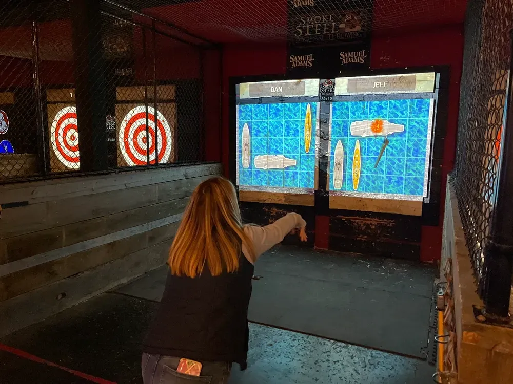 Woman throwing an axe at a digital target in an axe-throwing venue.
