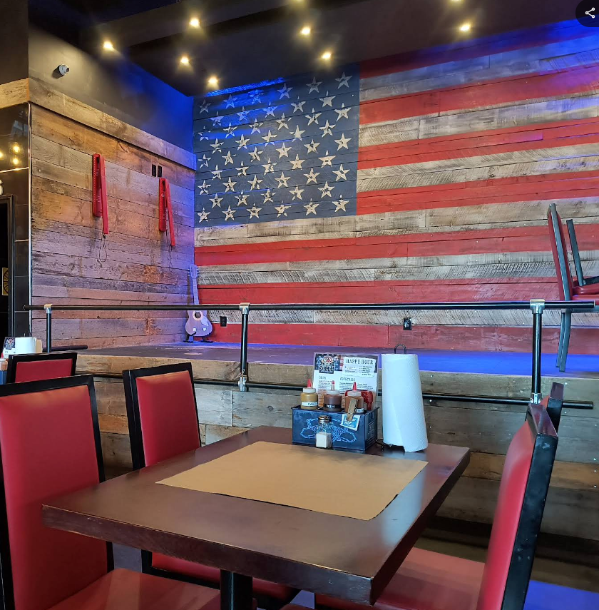Restaurant interior with an American flag mural and red chairs. Table set with paper, sauces.