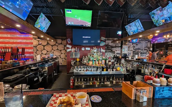 Interior of a bar, showing a bar with many liquor bottles, TVs, and a meal on the bar.