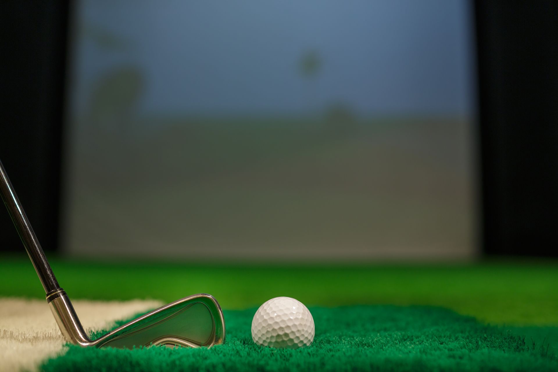 Golf club and ball on a green mat, with a screen in the background.
