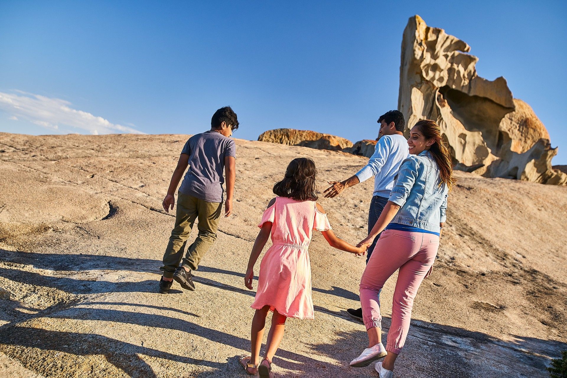 Family hiking up a rocky hill toward a rock formation; sunny day.