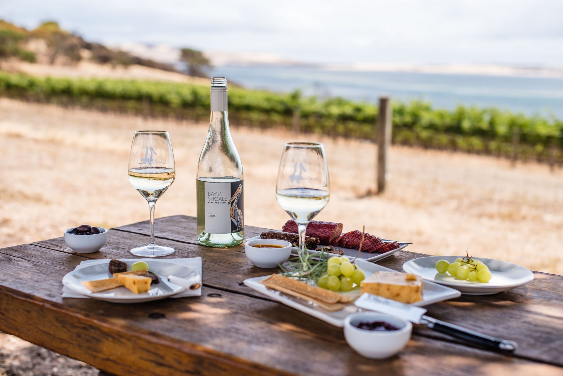 Table set with wine and snacks overlooking a vineyard and water.