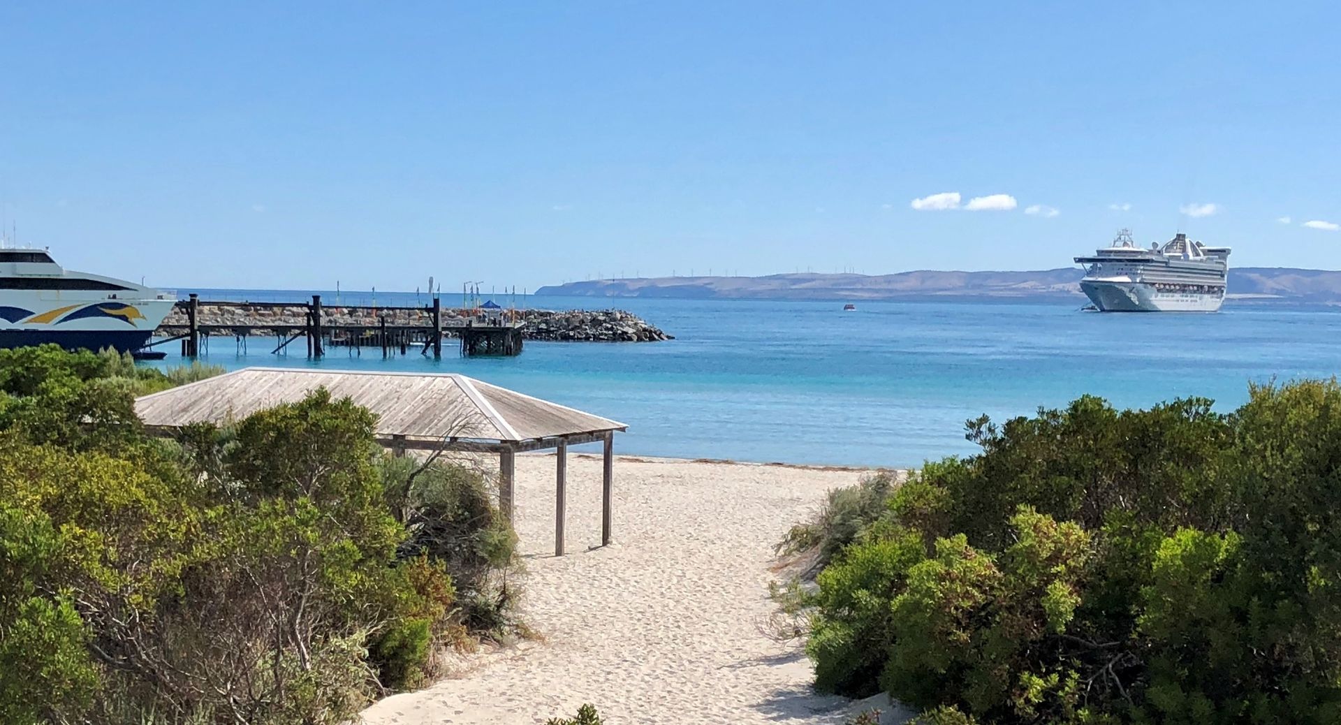 Beach scene with a cruise ship in the distance, pier, gazebo, and blue sky.