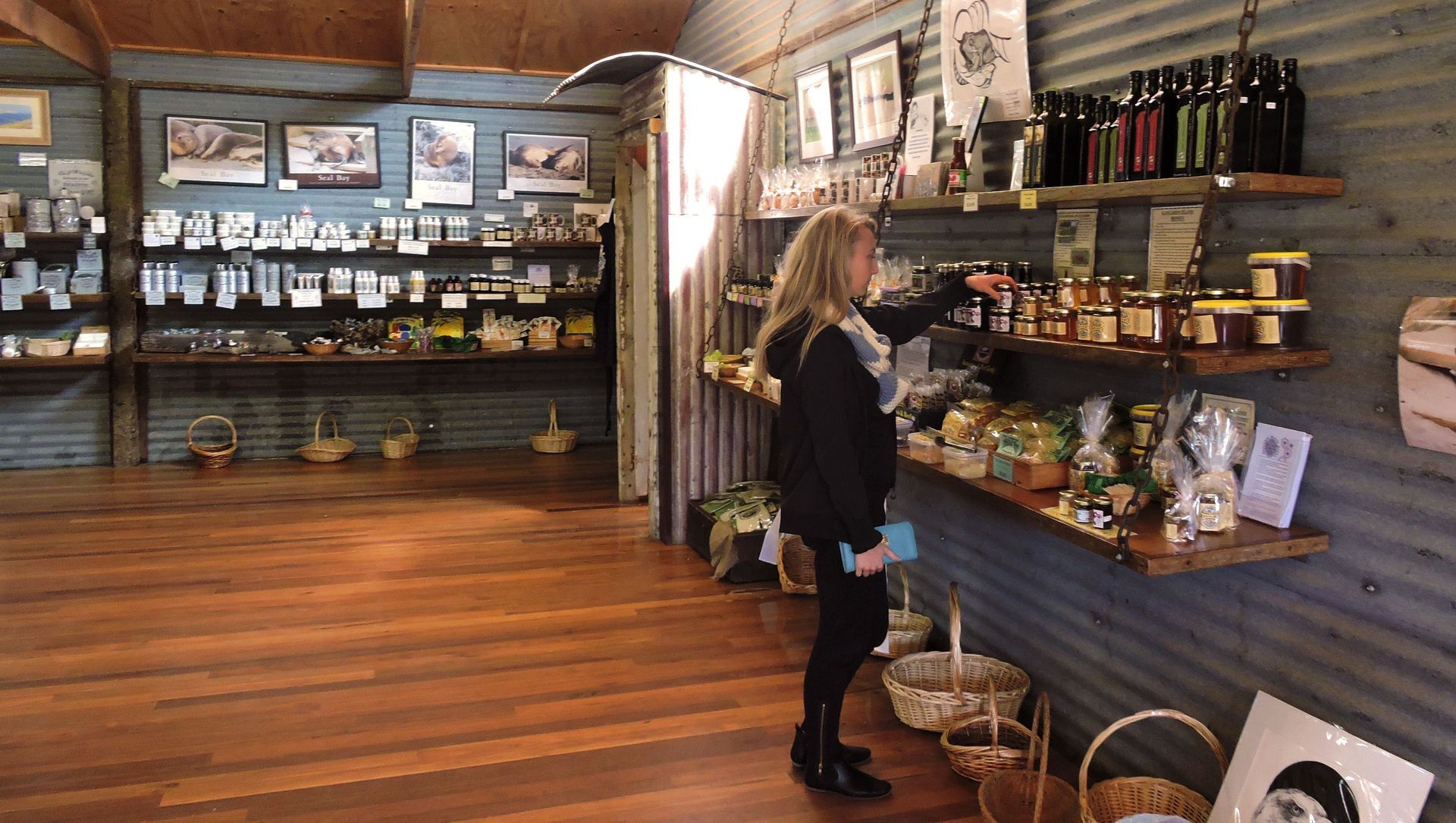 Woman browsing products on shelves in a rustic shop; wooden floors, metal siding walls.