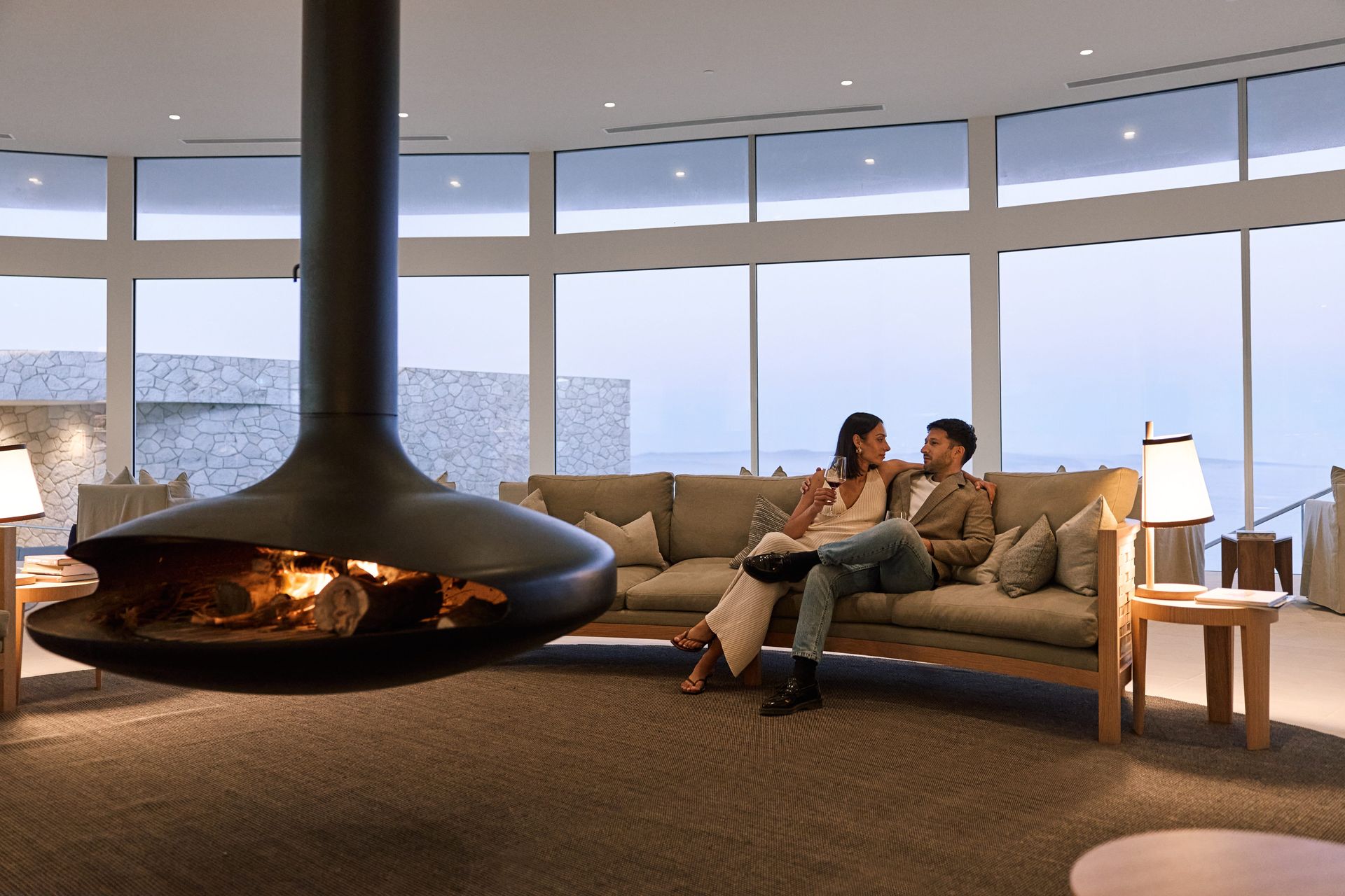 Couple relaxing on a sofa near a suspended fireplace, overlooking a scenic view.