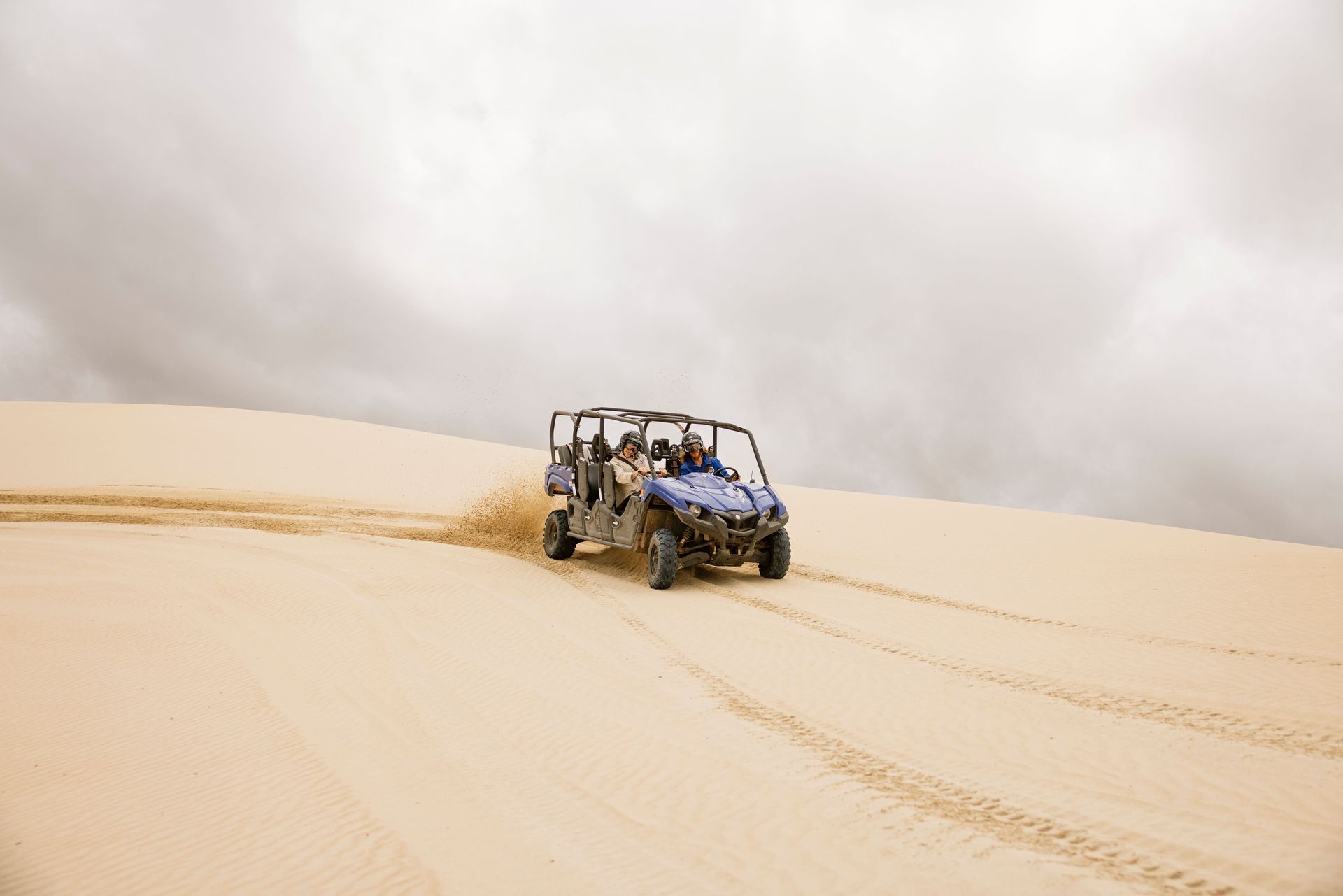 Off-road vehicle driving on a sand dune under a cloudy sky.