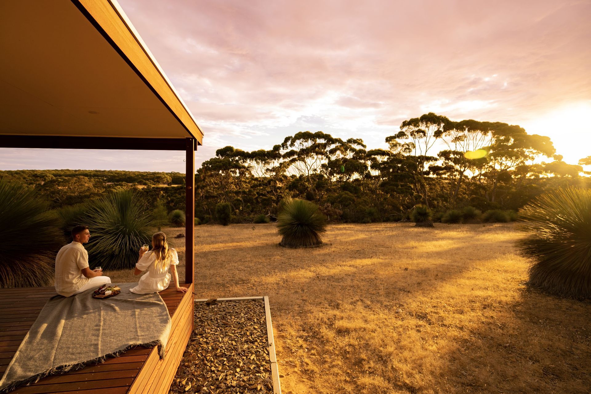 Couple on a porch enjoying sunset over Australian landscape.