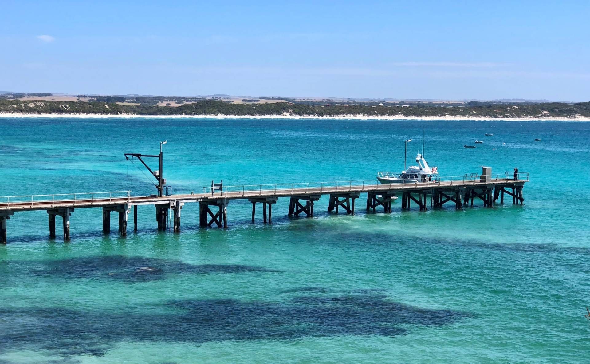 A pier extends into the turquoise ocean with a boat, under a blue sky, in a coastal setting.
