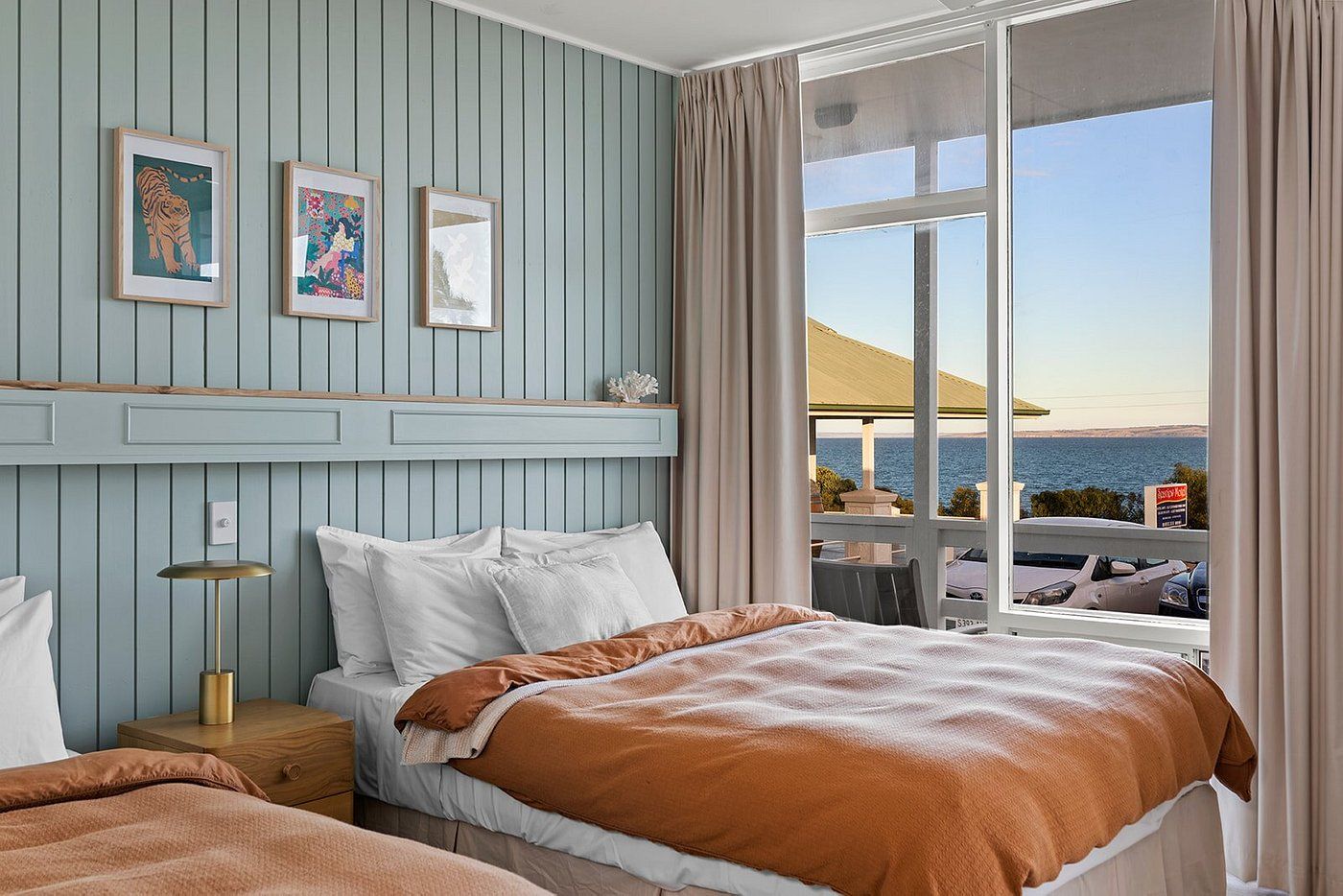 Bedroom with two beds, blue paneling, three framed pictures, and a view of the ocean.