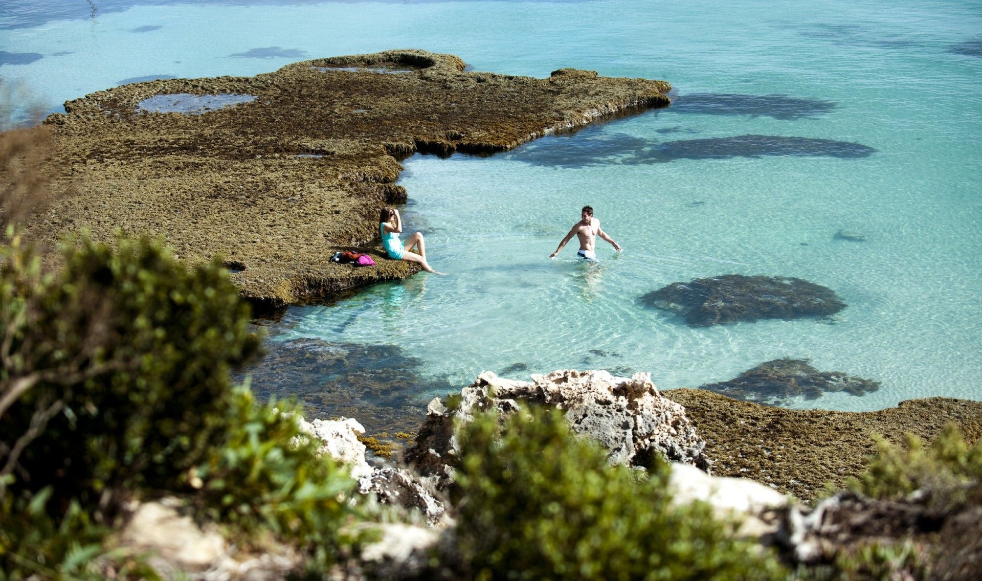 People in clear turquoise water near rocky shore.