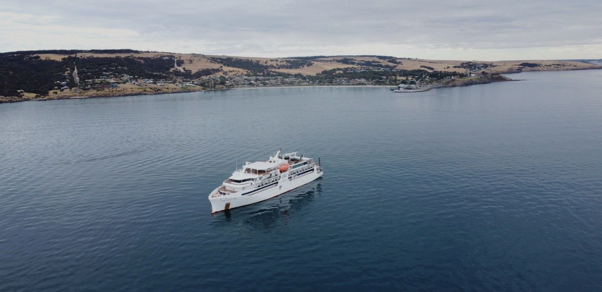 A white boat floats on blue water near a coastline under a cloudy sky.