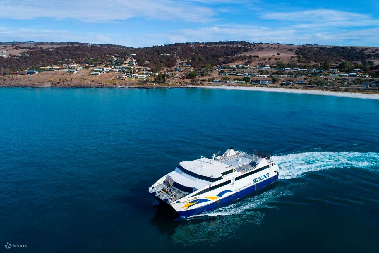 Ferry sailing on blue water towards a coastal town with a white sand beach.