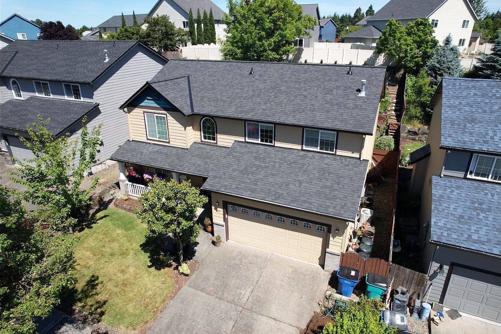 Aerial view of a two-story suburban house with gray roof, beige siding, driveway, and front yard.