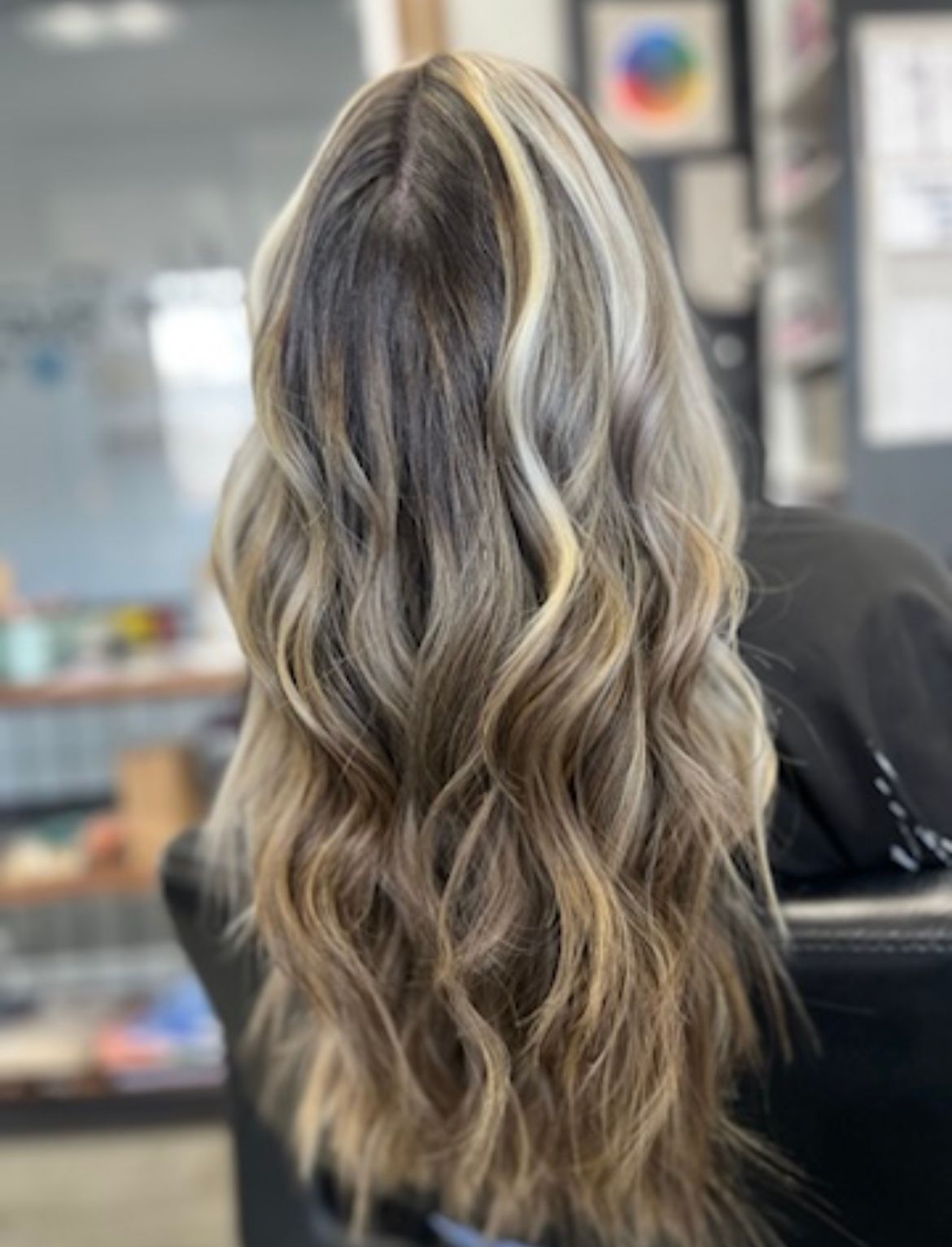 A woman with long wavy hair is sitting in a chair in a salon.