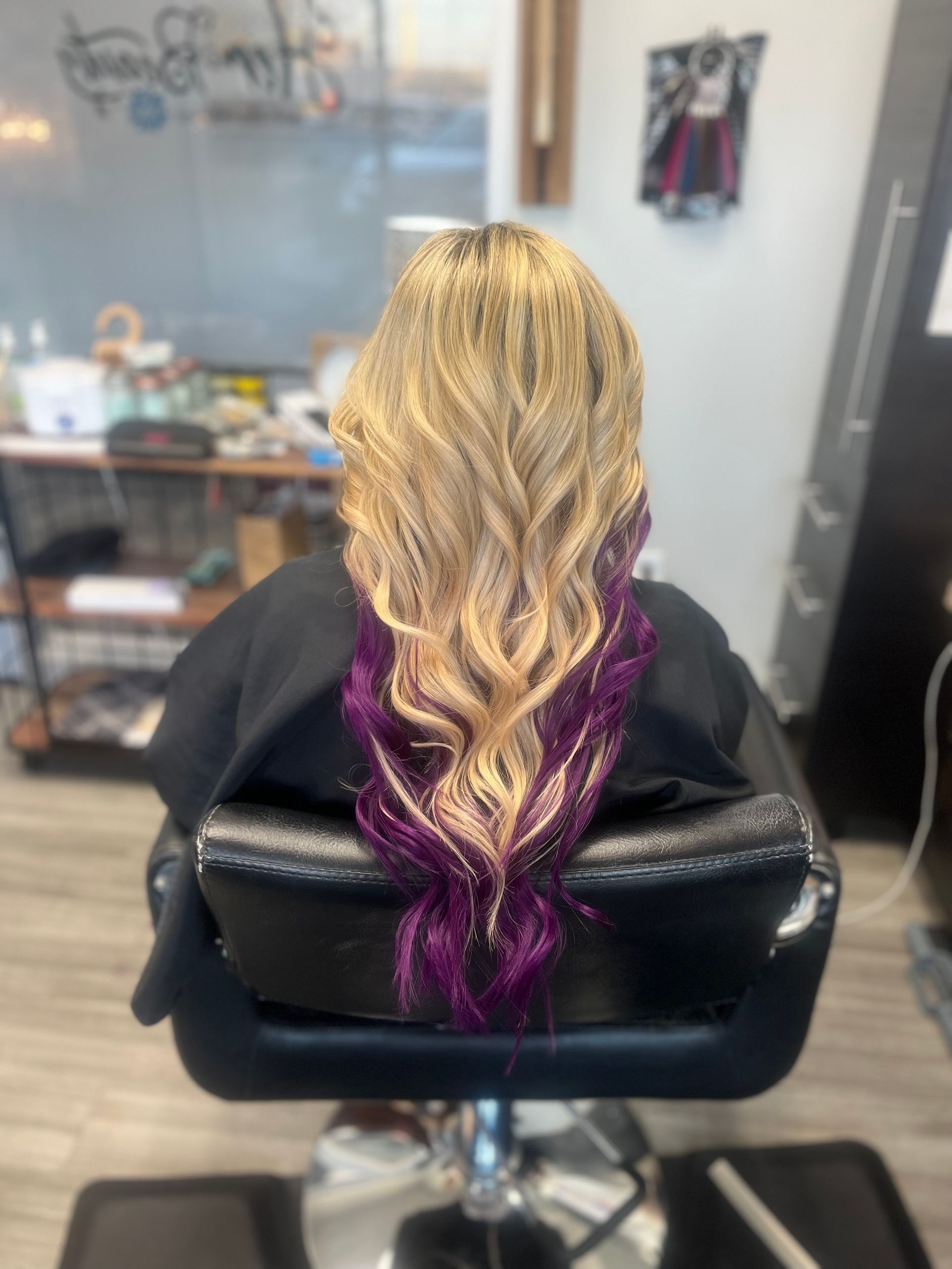 A woman is sitting in a chair with purple hair extensions.