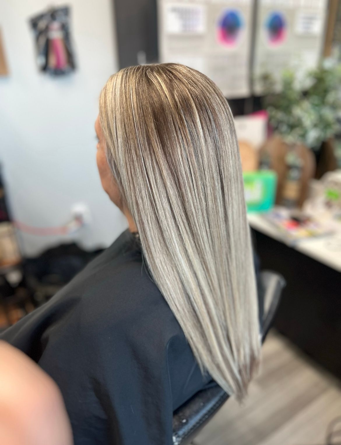A woman with long blonde hair is sitting in a chair in a salon.