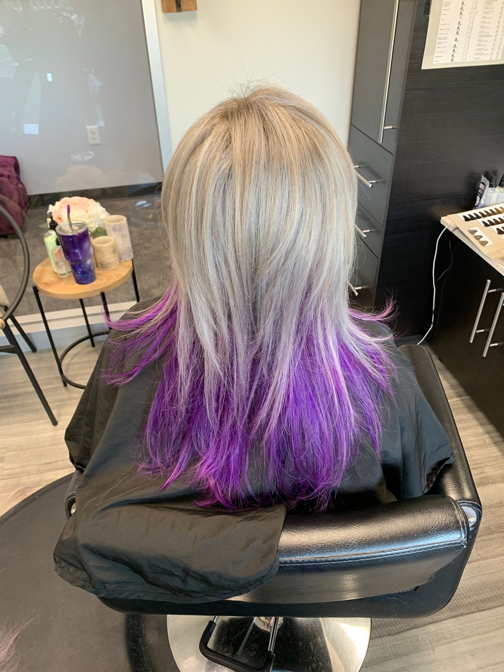 A woman is sitting in a chair with purple hair.