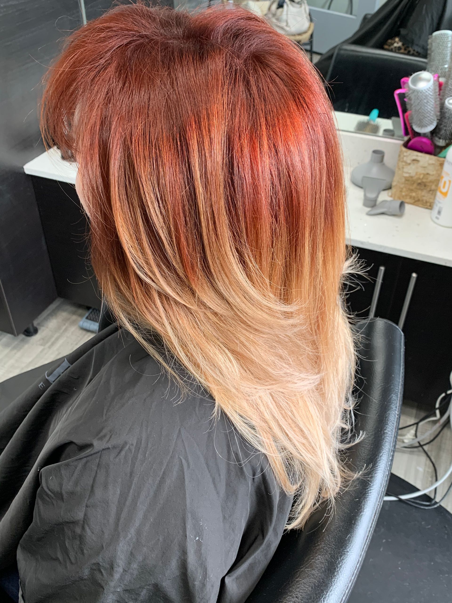 A woman with long red hair is sitting in a chair in a salon.