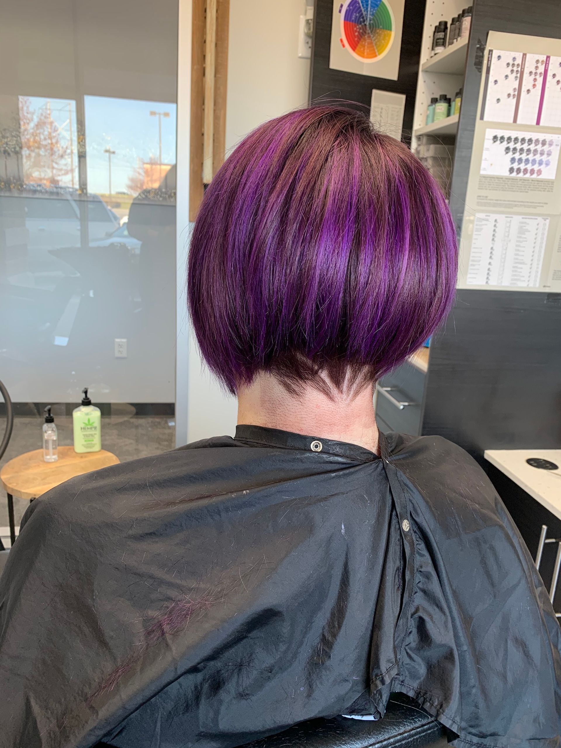 A woman with purple hair is sitting in a chair at a hair salon.