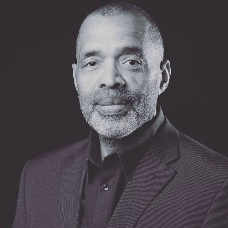 A man with a beard is wearing a suit and smiling in a black and white photo.