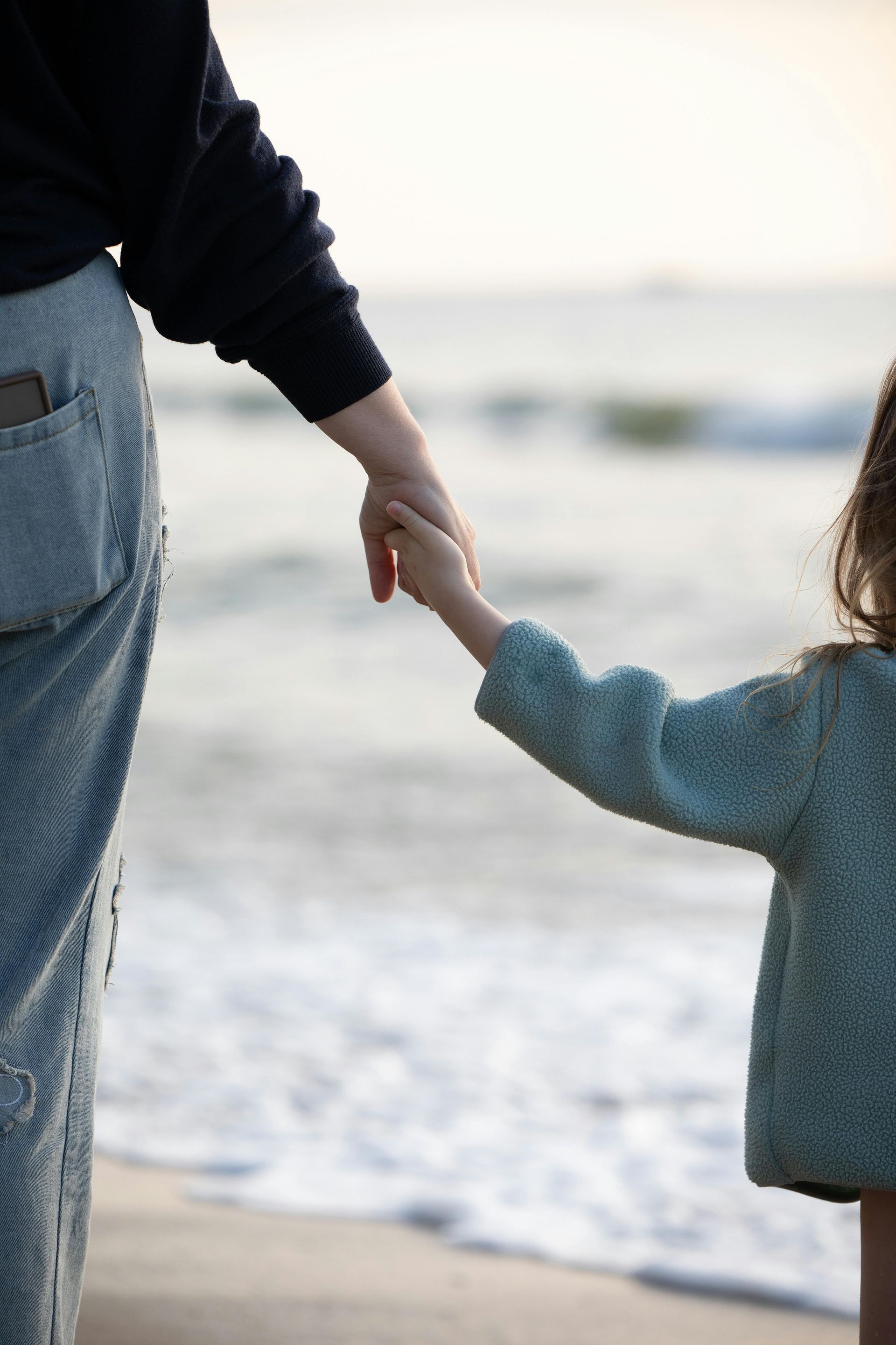 Adult and child holding hands on a beach with waves in the background